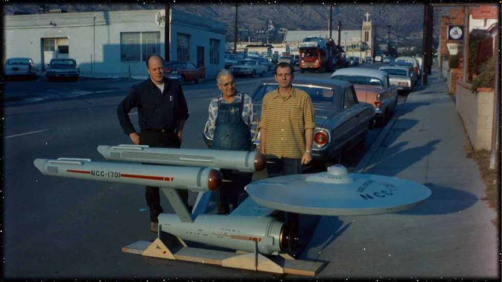 A group of people standing next to a model of a star trek Description automatically generated